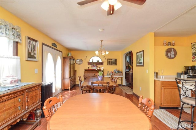dining room featuring dark wood-style flooring, a chandelier, a ceiling fan, and arched walkways