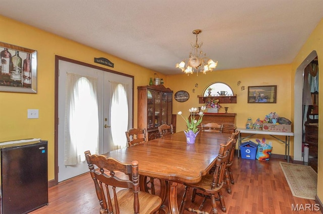 dining area featuring plenty of natural light, wood finished floors, a chandelier, and arched walkways