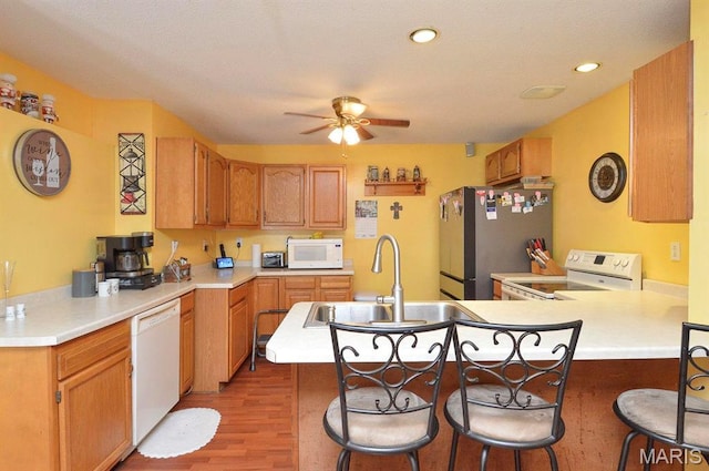 kitchen with white appliances, a sink, a peninsula, wood finished floors, and a ceiling fan