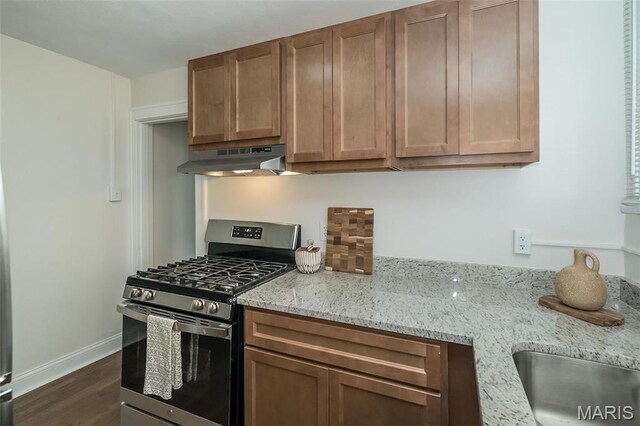 4117 Ravenwood Ave, Saint Louis, MO 63121 - kitchen featuring stainless steel gas range oven, under cabinet range hood, dark wood-type flooring, light stone counters, and baseboards