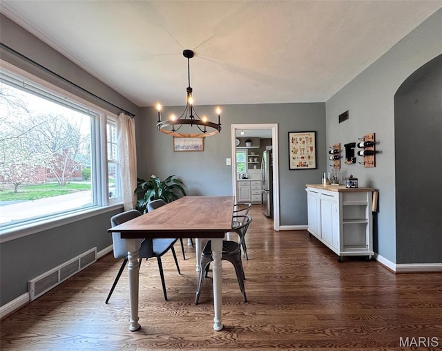 dining area with a chandelier, dark wood finished floors, arched walkways, and baseboards