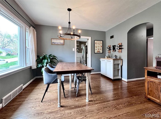 dining space featuring arched walkways, dark wood-style flooring, healthy amount of natural light, and a chandelier