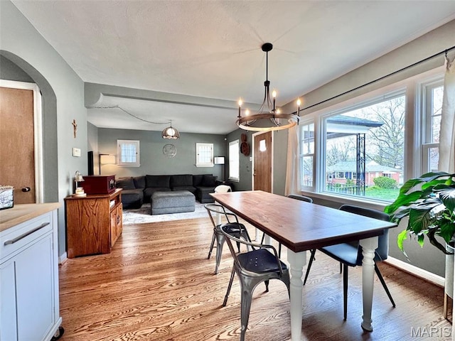 dining space featuring light wood-style flooring, baseboards, a chandelier, and arched walkways