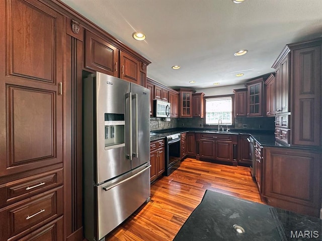 15012 Bay Hills Dr, Dexter, MO 63841 - kitchen with stainless steel appliances, a sink, decorative backsplash, glass insert cabinets, and wood finished floors