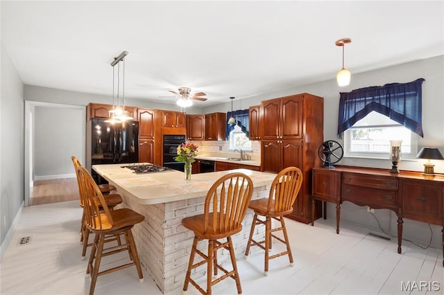 kitchen featuring black appliances, tasteful backsplash, ceiling fan, light countertops, and a breakfast bar area