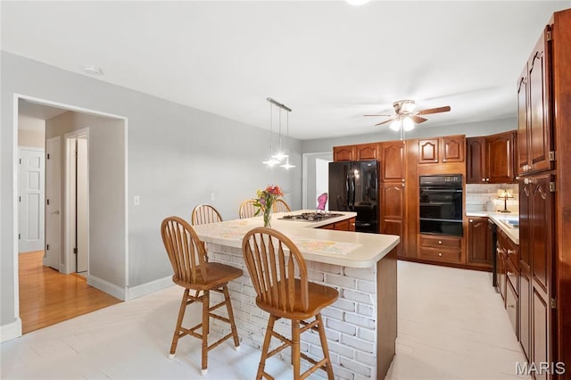 kitchen with black appliances, a warming drawer, light countertops, a breakfast bar area, and a ceiling fan