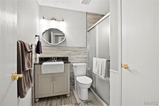 full bath featuring wood finished floors, a shower stall, toilet, vanity, and tile walls