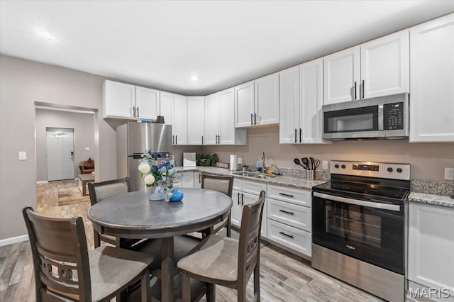 1428 Mallinckrodt, Saint Louis, MO 63107 - kitchen with stainless steel appliances, a sink, light wood-style floors, white cabinets, and recessed lighting