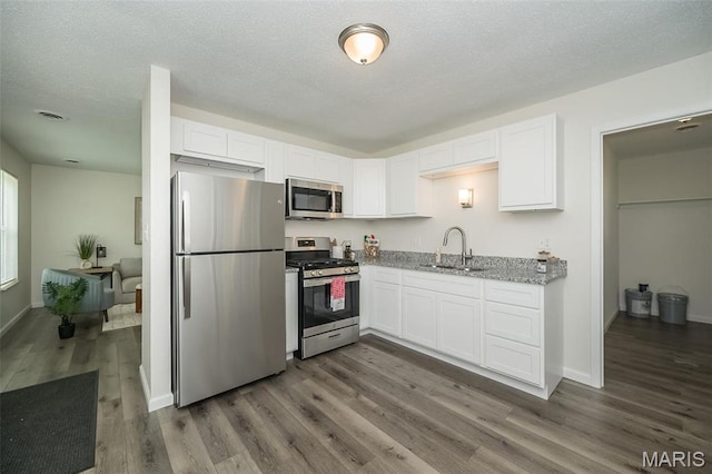 1331 Belrue Ave, Saint Louis, MO 63133 - kitchen with appliances with stainless steel finishes, a sink, white cabinets, dark wood-style floors, and a textured ceiling