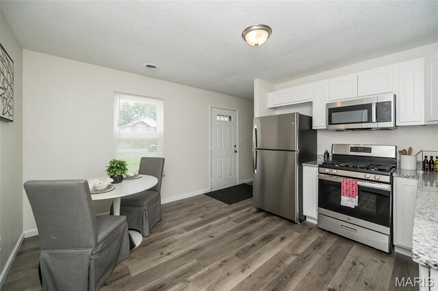 1331 Belrue Ave, Saint Louis, MO 63133 - kitchen with stainless steel appliances, wood finished floors, white cabinetry, light stone countertops, and a textured ceiling