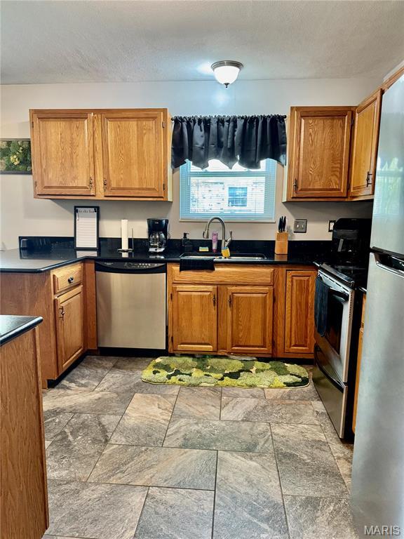 1725 Spruce Hill Dr, Belleville, IL 62221 - kitchen featuring appliances with stainless steel finishes, a sink, brown cabinets, and light stone finish flooring