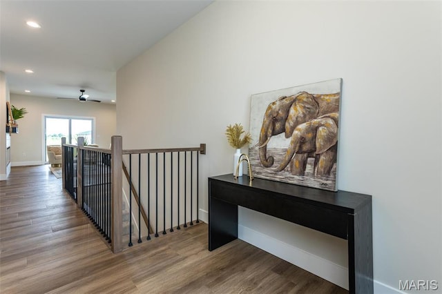 hallway with an upstairs landing, wood finished floors, recessed lighting, and baseboards