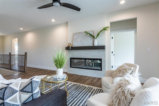 living area with wood finished floors, recessed lighting, ceiling fan, a tiled fireplace, and baseboards