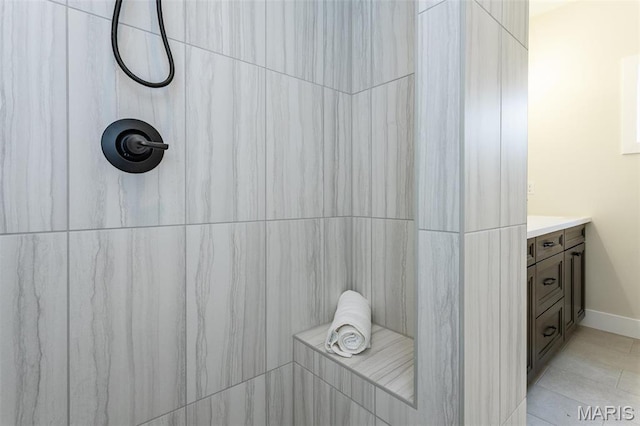 bathroom with a tile shower, vanity, and baseboards