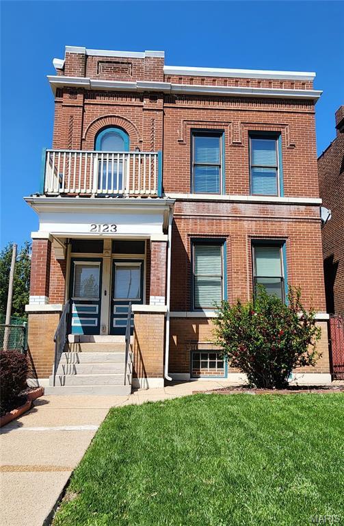 view of front of property featuring a balcony, brick siding, and a front yard