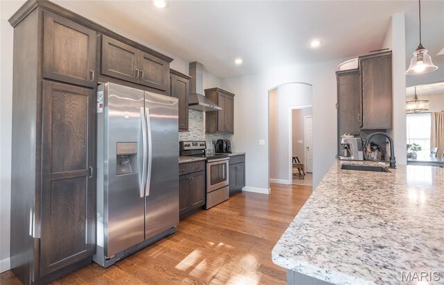 1347 Thomas Dr, Rolla, MO 65401 - kitchen featuring stainless steel appliances, wall chimney range hood, a sink, arched walkways, and backsplash