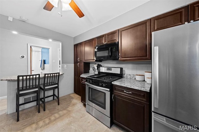 8452 S Laclede Station Rd, Saint Louis, MO 63123 - kitchen with appliances with stainless steel finishes, ceiling fan, dark brown cabinets, light stone counters, and tile walls