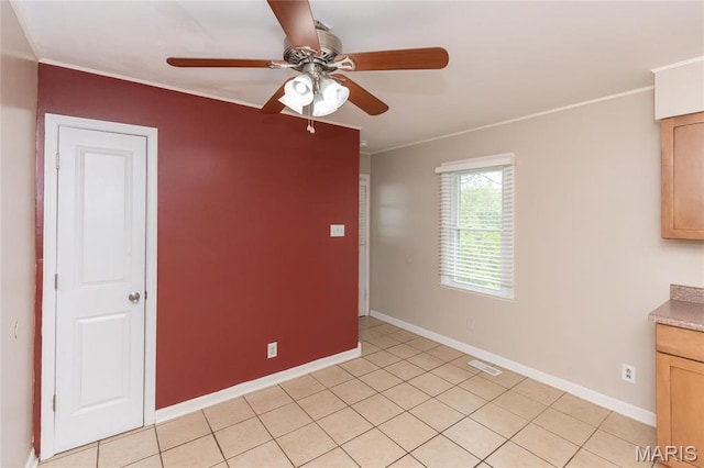 spare room with a ceiling fan, ornamental molding, baseboards, and light tile patterned floors
