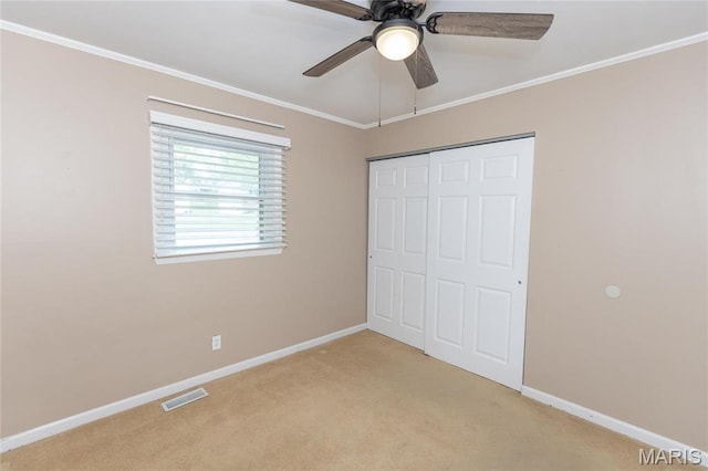 unfurnished bedroom featuring light colored carpet, baseboards, crown molding, a closet, and a ceiling fan