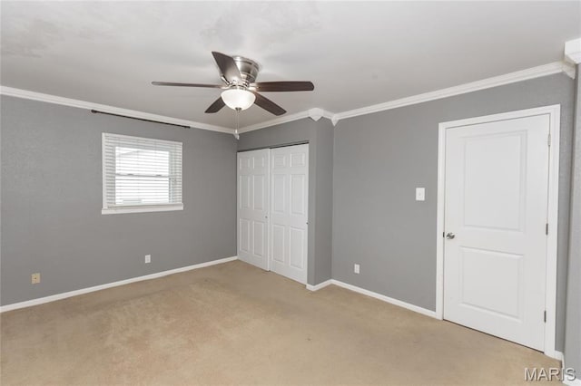 unfurnished bedroom featuring crown molding, light colored carpet, baseboards, a ceiling fan, and a closet