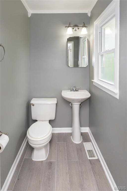 half bath with baseboards, toilet, wood tiled floors, and a sink