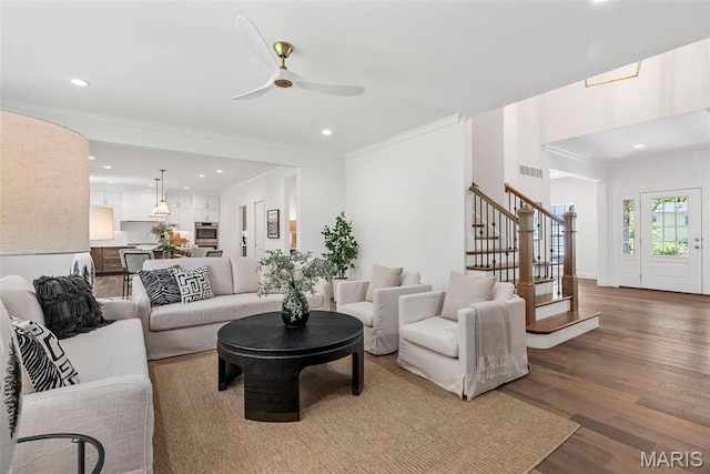 living area with stairway, recessed lighting, wood finished floors, ceiling fan, and ornamental molding