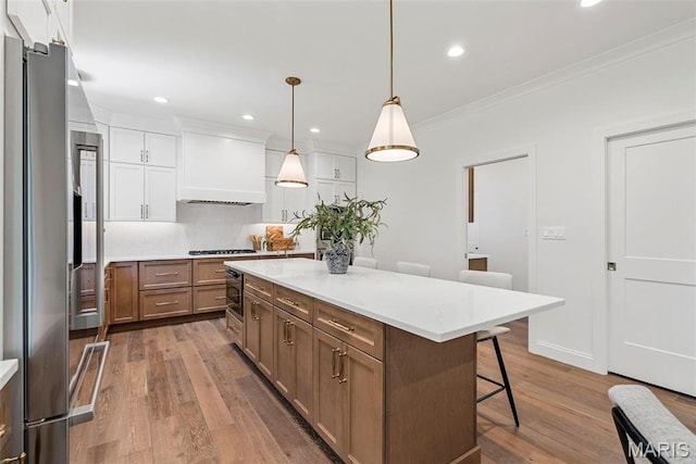 kitchen featuring stainless steel fridge, a kitchen breakfast bar, light wood-type flooring, crown molding, and white cabinetry