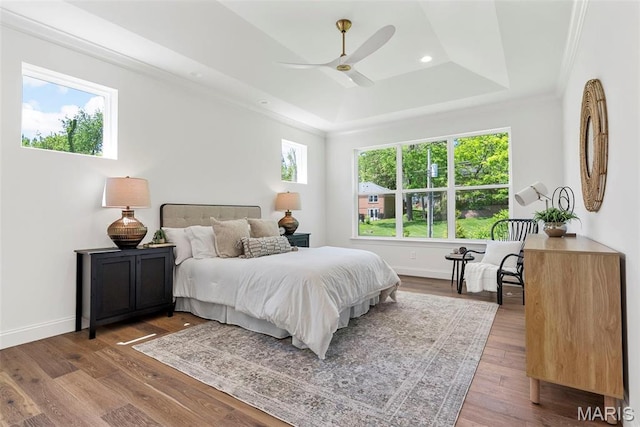 bedroom with a tray ceiling, baseboards, wood finished floors, crown molding, and recessed lighting
