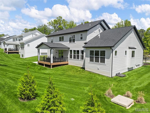 rear view of house featuring a wooden deck, a yard, and a shingled roof