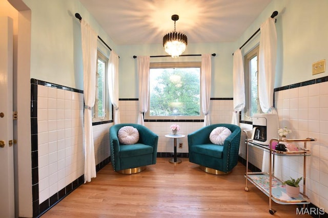 sitting room featuring tile walls, a wainscoted wall, plenty of natural light, light wood-style floors, and a chandelier