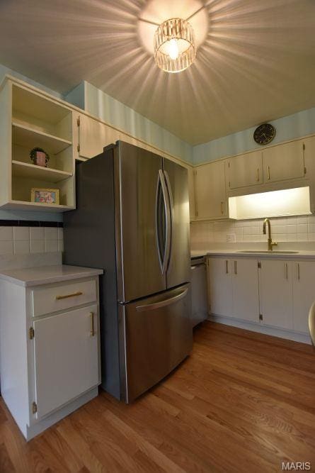 kitchen with a sink, light countertops, appliances with stainless steel finishes, decorative backsplash, and light wood-type flooring