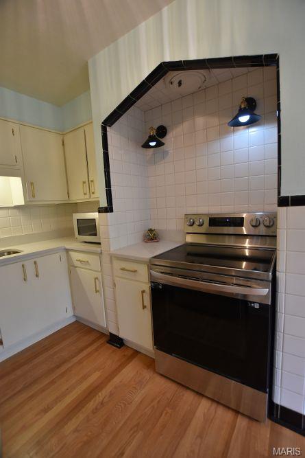 kitchen featuring electric range, light countertops, decorative backsplash, light wood-type flooring, and a sink