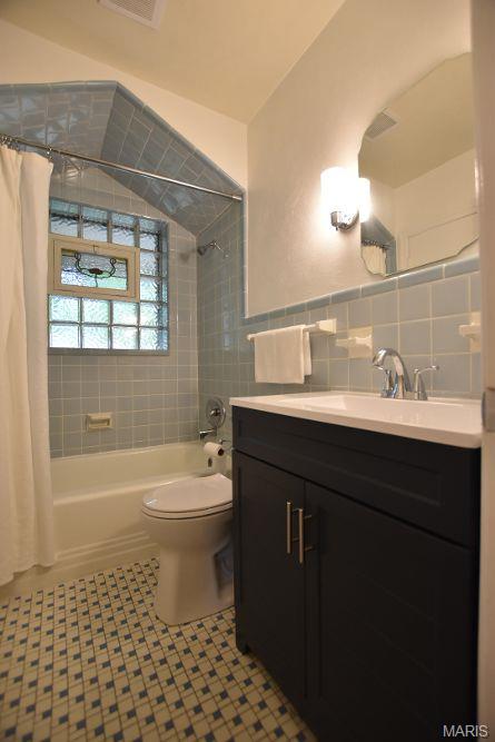 full bathroom with tile walls, shower / tub combo with curtain, toilet, vanity, and tile patterned floors