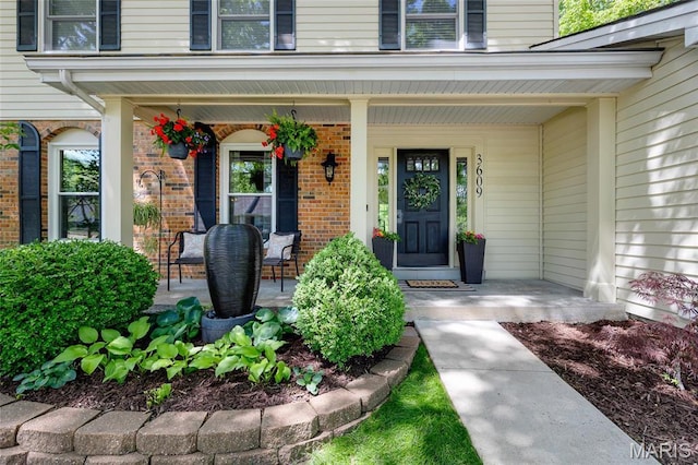 doorway to property featuring a porch and brick siding