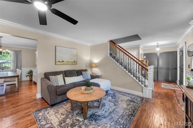 living room featuring wood finished floors, ornamental molding, a ceiling fan, and stairs