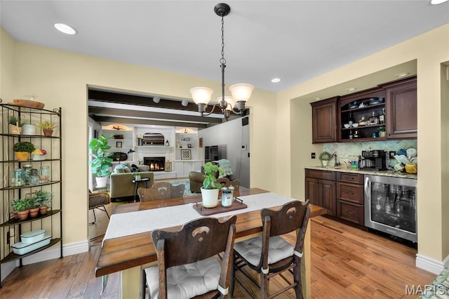dining area featuring wine cooler, bar area, light wood-type flooring, a chandelier, and a large fireplace