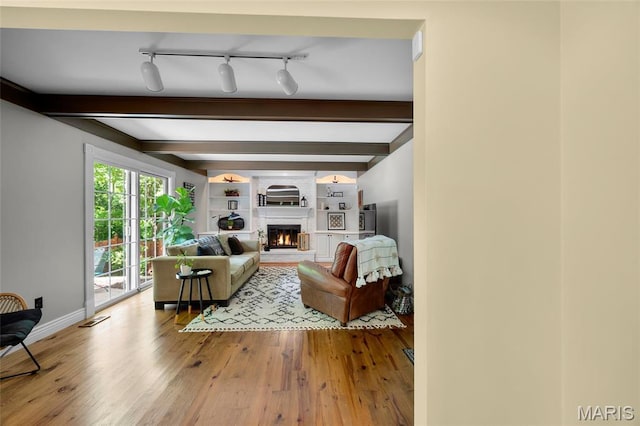 living area featuring wood finished floors, a fireplace, beam ceiling, baseboards, and track lighting
