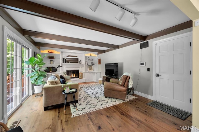 living area with baseboards, beam ceiling, light wood finished floors, a fireplace, and track lighting