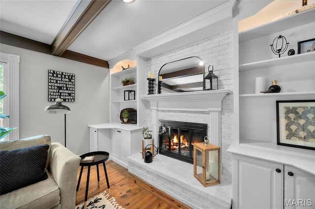 living area with a fireplace, wood finished floors, built in shelves, and beamed ceiling