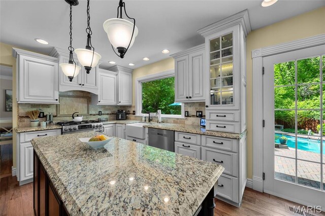 kitchen with stainless steel appliances, a sink, white cabinets, tasteful backsplash, and glass insert cabinets