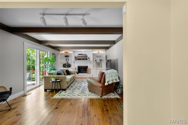living area with wood finished floors, beamed ceiling, baseboards, a fireplace, and rail lighting