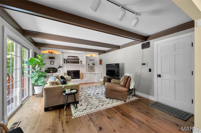 living area featuring beamed ceiling, baseboards, wood finished floors, a fireplace, and track lighting