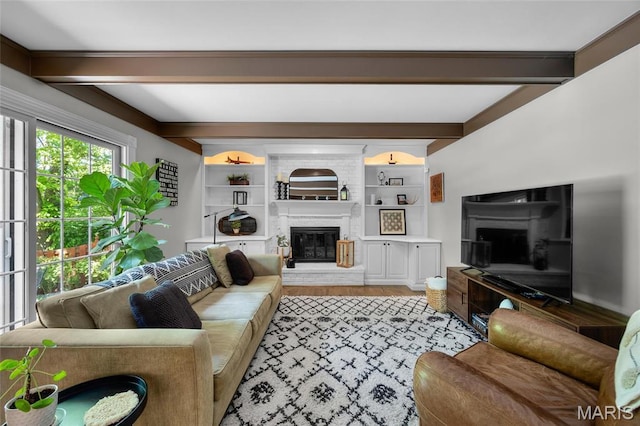 living area featuring a brick fireplace, beam ceiling, and wood finished floors