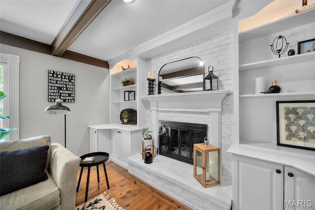 living room featuring wood finished floors, a fireplace, beamed ceiling, built in shelves, and ornamental molding