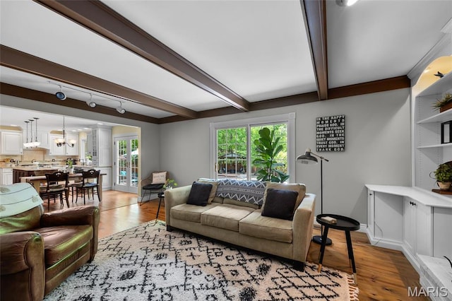 living room featuring light wood-style flooring, plenty of natural light, beam ceiling, and baseboards