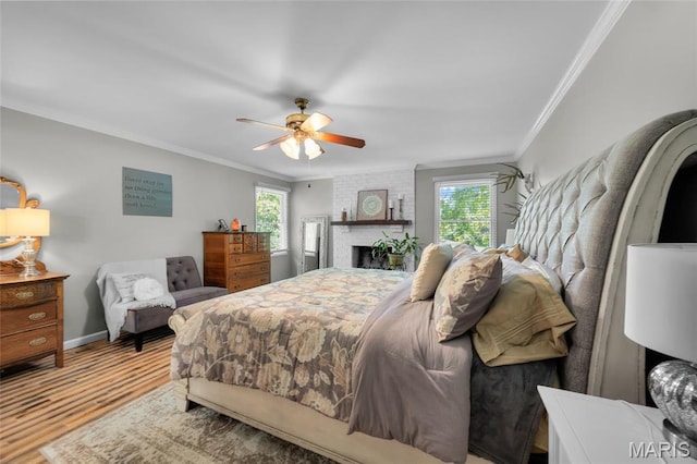 bedroom with crown molding, wood finished floors, baseboards, ceiling fan, and a brick fireplace