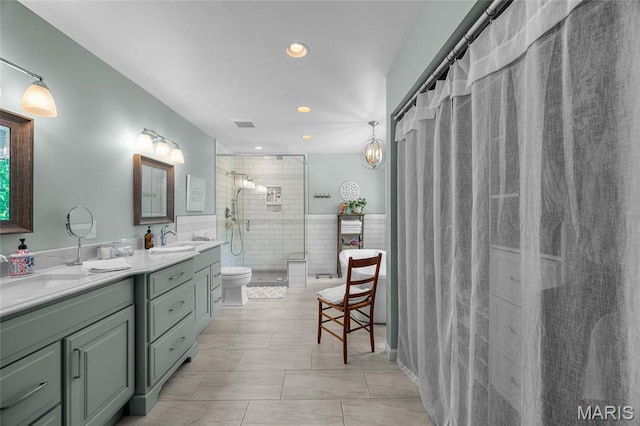 bathroom featuring tile walls, a stall shower, recessed lighting, double vanity, and toilet