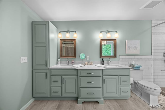 bathroom with toilet, double vanity, tile walls, a tile shower, and wood finished floors