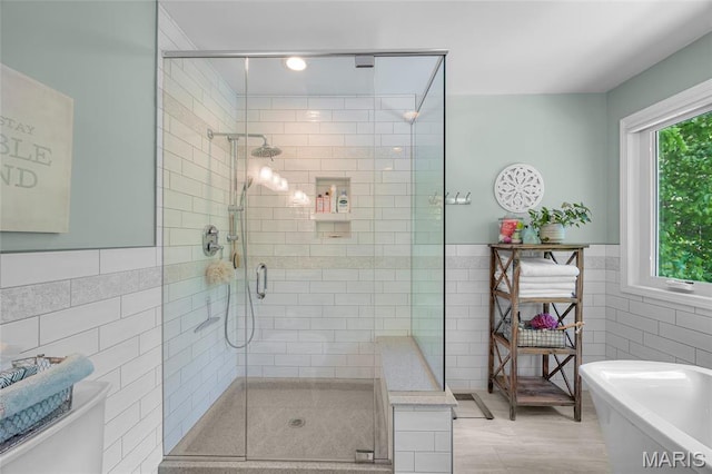 bathroom featuring tile walls, a freestanding tub, a shower stall, toilet, and wainscoting