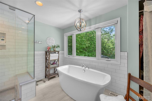 full bath with tile walls, tiled shower, a freestanding bath, a chandelier, and a wainscoted wall